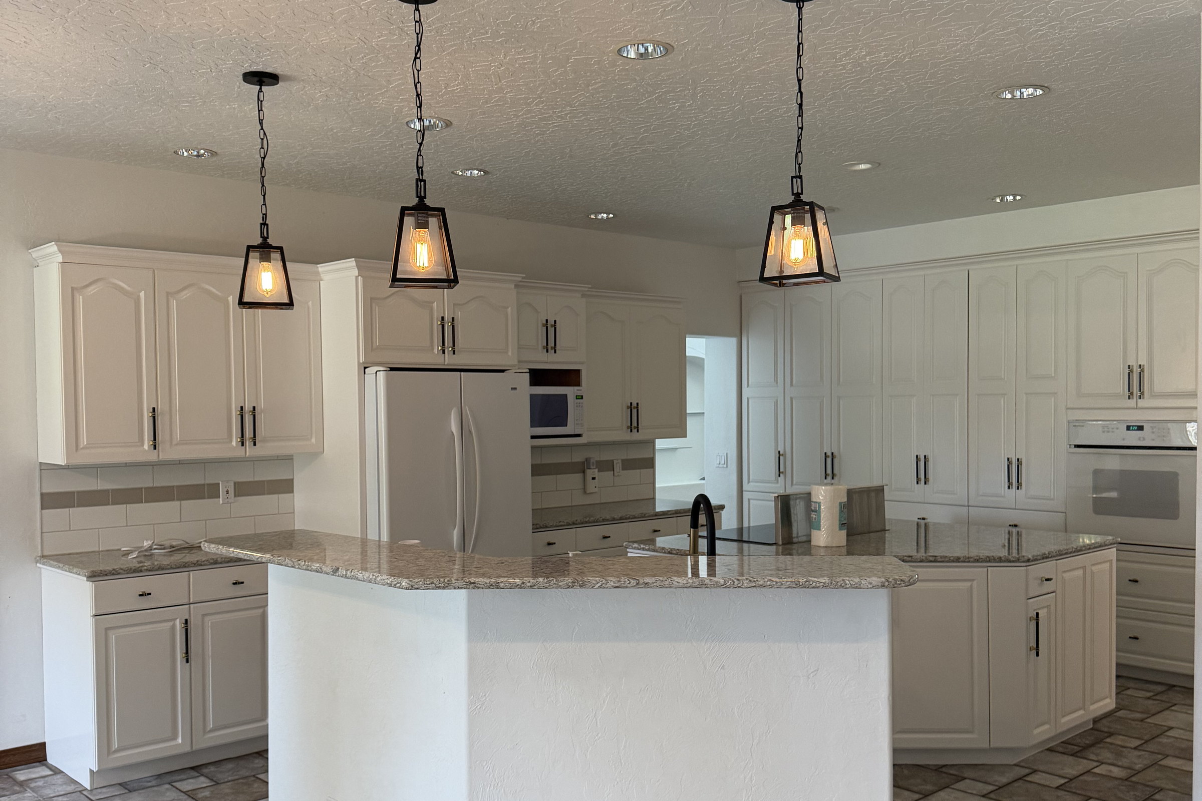 Original kitchen with white raised panel cabinets, a stone topped angled island, white appliances and tile flooring.
