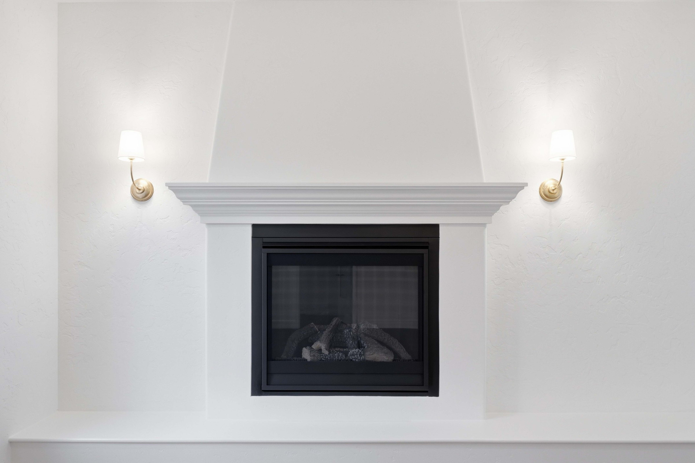 Remodeled fireplace wall with a white plaster surround, a profiled mantel and brass sconces in place of the built ins.