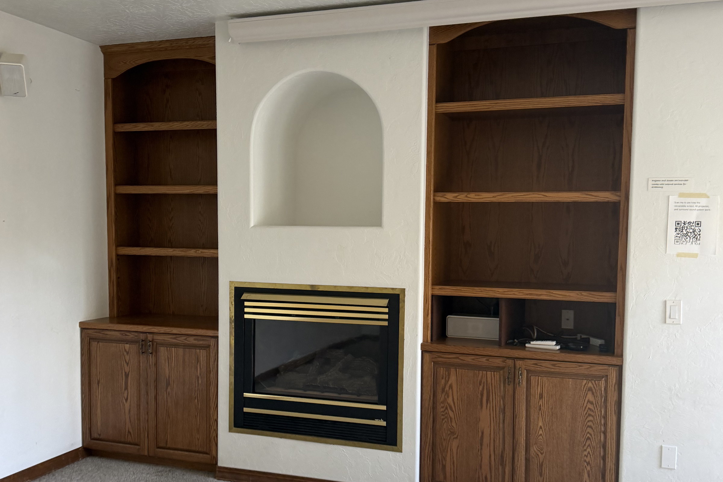 Original living room fireplace with a brass trimmed firebox, an arched plaster niche above and oak built in shelving on both sides.