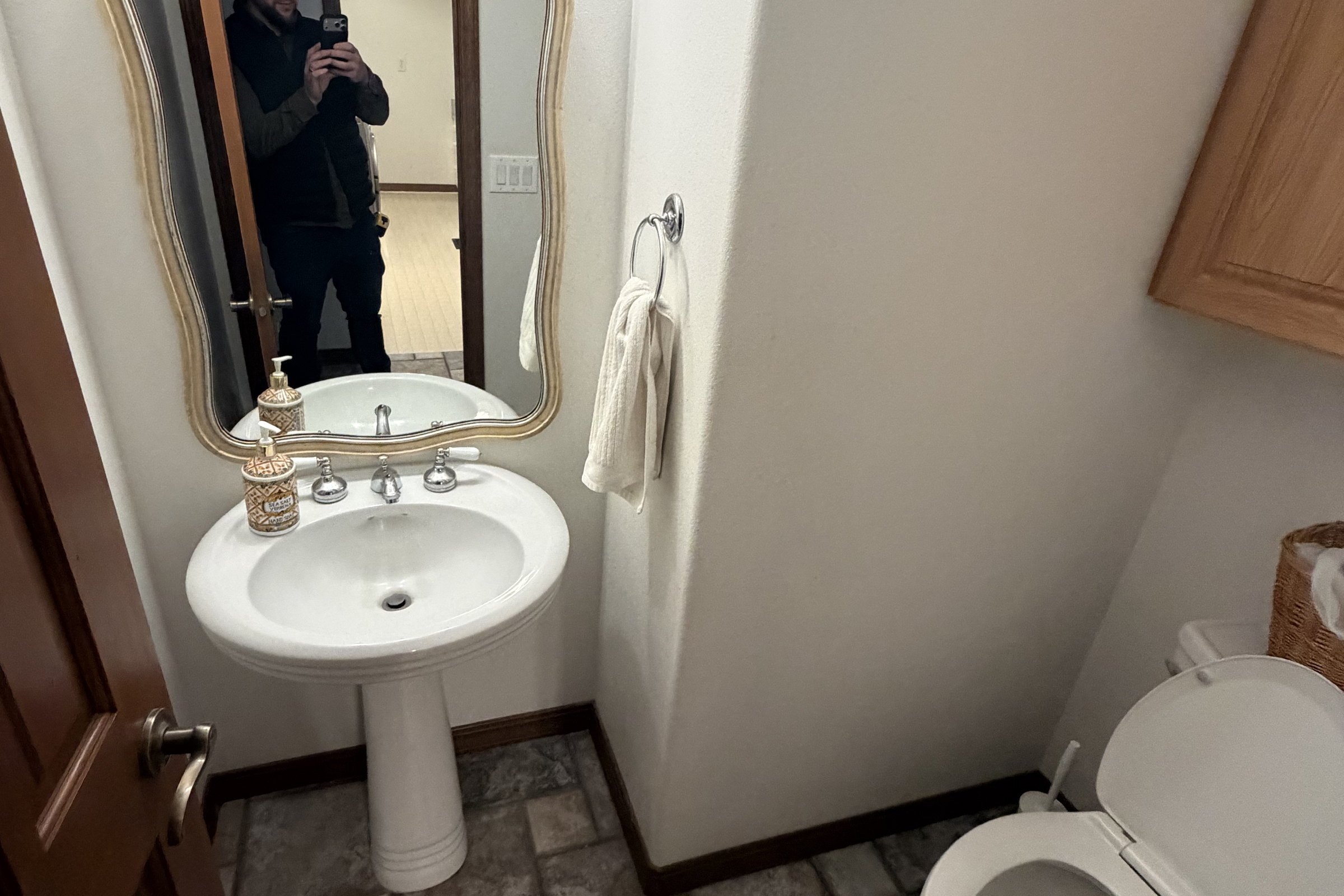 Original powder bathroom with a pedestal sink, a gold scalloped mirror and stone look tile laid in a brick pattern.