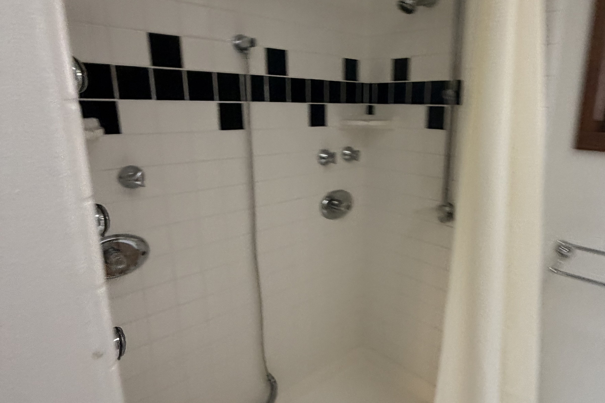 Original shower alcove tiled in white square tile with a black accent band and a shower curtain.